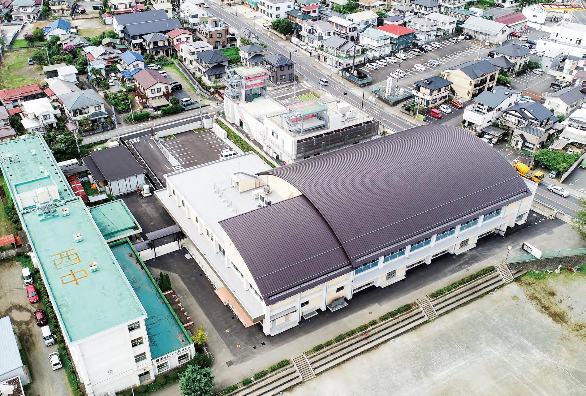 上空から捉えられた、茶色いかまぼこ型の屋根を持つ大きな体育館と、隣接する校舎や周辺の住宅街が広がる写真