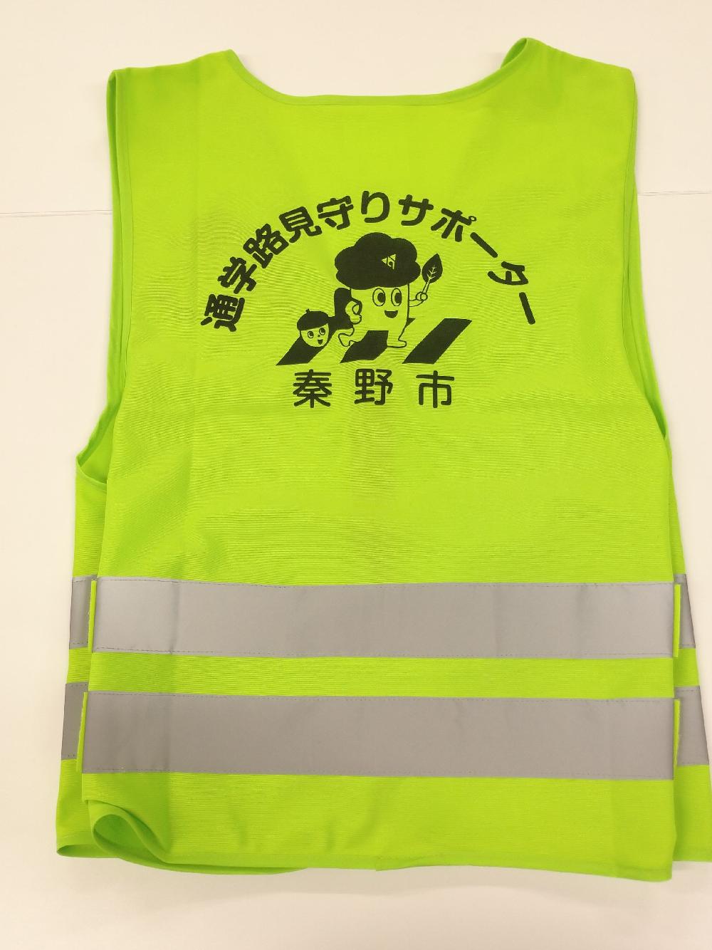 蛍光イエローの安全ベストの背面で、中央には「通学路見守りサポーター」と書かれその下に横断歩道をランドセルを背負ったもりりんが渡っているイラストが描かれた写真