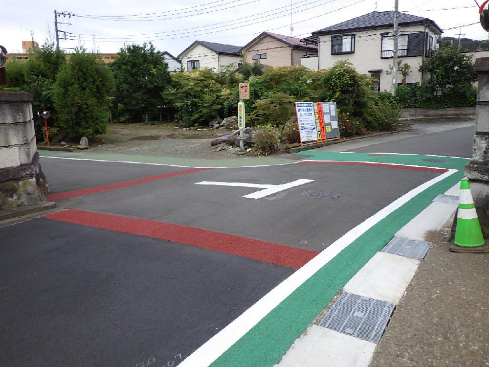住宅地の交差点で、赤色と緑色のカラー舗装が白い太線で区切られ、中央にT字が路面標示されている道路の写真