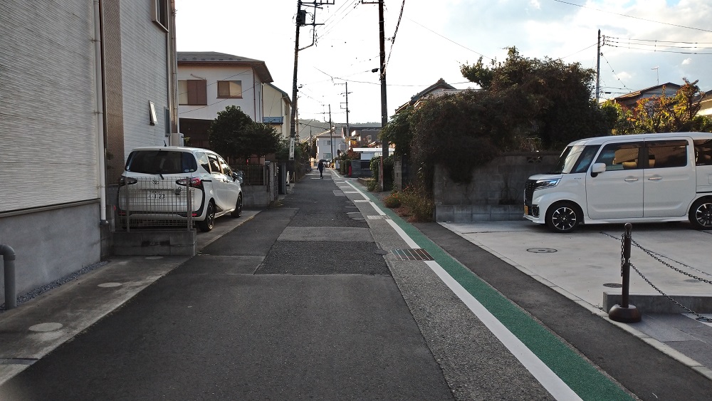 住宅街の細い道に緑色と白のラインが引かれたアスファルトの道が奥へと続いている写真