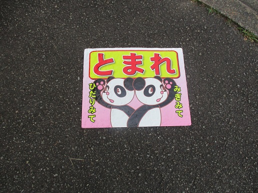 アスファルトの路上に貼られた、ピンク色の背景に可愛らしいパンダが描かれ、上部に「とまれ」、左右にそれぞれ「ひだりみて」「みぎみて」と交通安全を促す文字が記されている注意喚起のイラスト