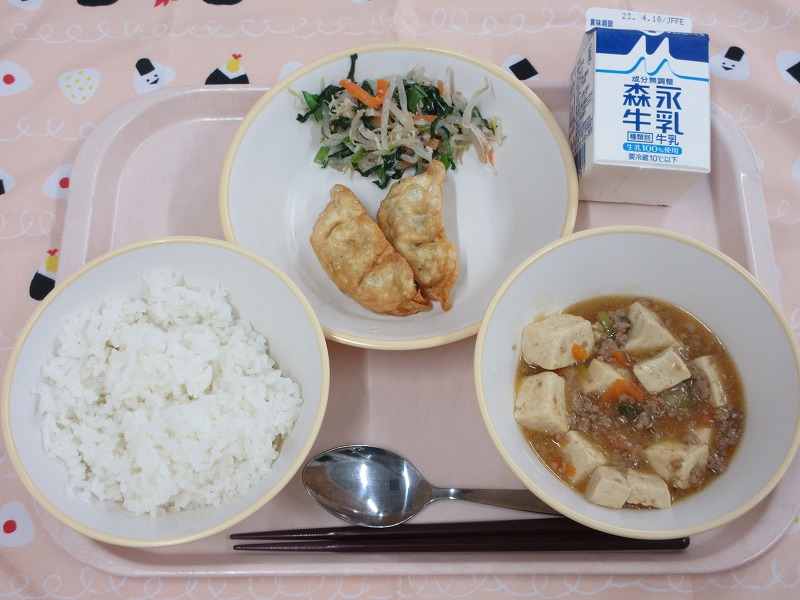 ピンクのトレーに給食が右上から反時計回りで牛乳、揚げ餃子とささみ入りナムル、ご飯、麻婆豆腐と並べられている写真