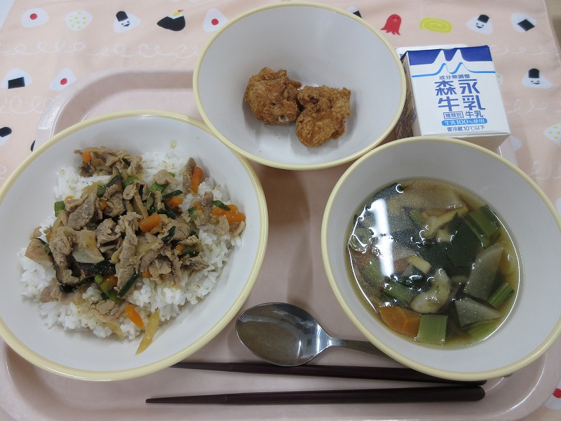 ピンクのトレーに給食が右上から反時計回りで牛乳、秦野の桜ボールドーナツ、焼肉ごはん（麦入りご飯）、根菜汁と並べられている写真