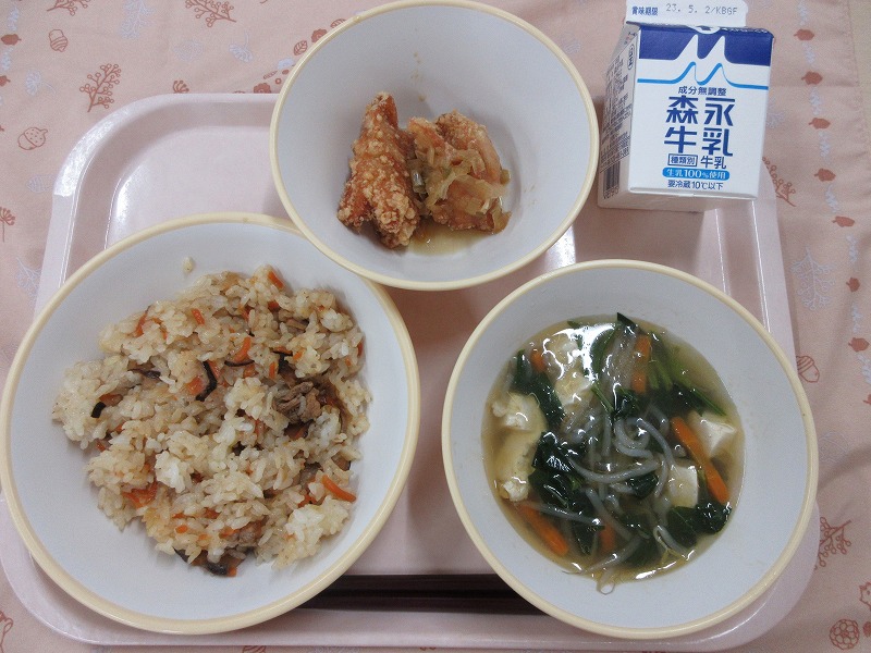 ピンクのトレーに給食が右上から反時計回りで牛乳、油淋鶏、中華風おこわ、五目スープと並べられている写真