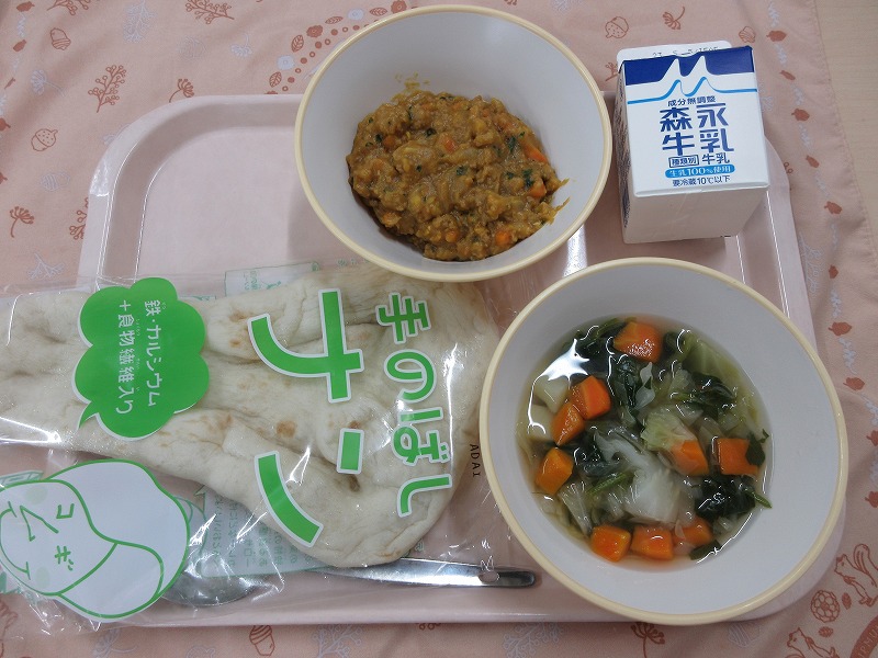 ピンクのトレーに給食が右上から反時計回りで牛乳、ドライカレー、ナン、野菜スープと並べられている写真