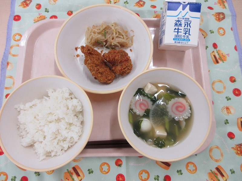 ピンクのトレーに給食が右上から反時計回りで牛乳、鶏肉のお茶の葉フライとピリ辛もやし、ご飯、白玉汁と並べられている写真