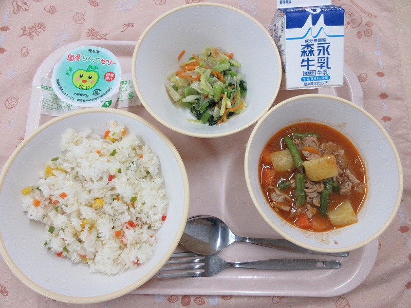 ピンクのトレーに給食が右上から反時計回りで牛乳、しらたきサラダ、りんごゼリー、カラフルピラフ、ポークシチューと並べられている写真