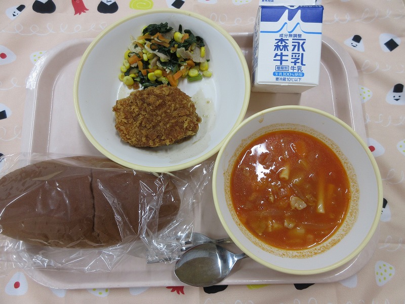 ピンクのトレーに給食が右上から反時計回りで牛乳、コロッケとコーンソテー、黒パン、ミネストローネと並べられている写真
