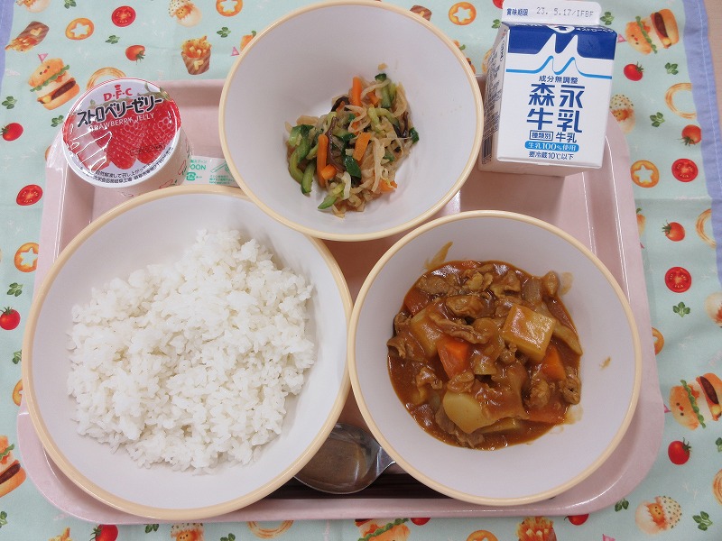 ピンクのトレーに給食が右上から反時計回りで牛乳、切り干し大根のサラダ、いちごゼリー、ご飯、カレーライスと並べられている写真