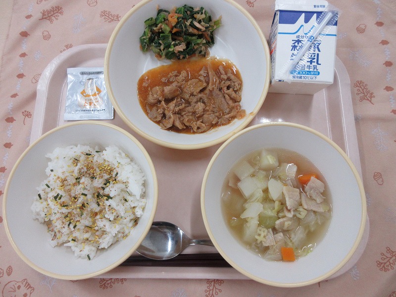 ピンクのトレーに給食が右上から反時計回りで牛乳、豚肉のトマみそ炒めとこまツナサラダ、ご飯（ふりかけ）、ABCスープと並べられている写真