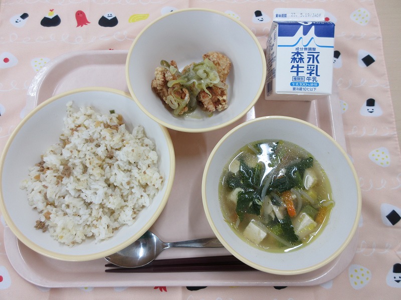 ピンクのトレーに給食が右上から反時計回りで牛乳、鶏肉のねぎ塩だれかけ、チャーハン風まぜごはん、豆腐の中華スープと並べられている写真