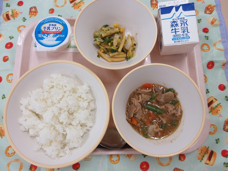 ピンクのトレーに給食が右上から反時計回りで牛乳、ミックスサラダ、牛乳プリン、ご飯、豚丼の具と並べられている写真