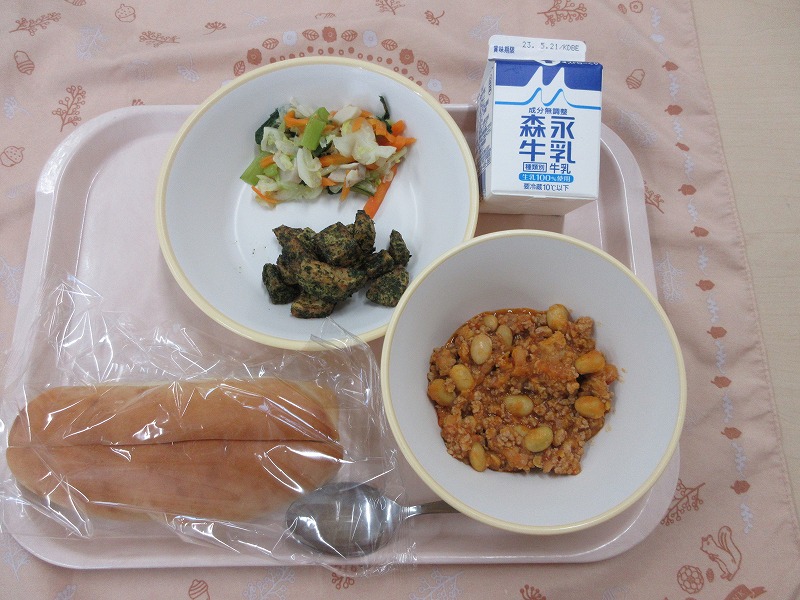 ピンクのトレーに給食が右上から反時計回りで牛乳、青のりポテトと野菜ソテー、ソフトフランスパン、チリコンカンと並べられている写真