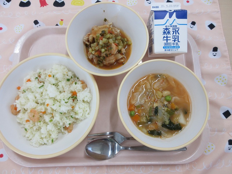 ピンクのトレーに給食が右上から反時計回りで牛乳、揚げ鶏のラピゴットソース、えびピラフ、リボリータと並べられている写真