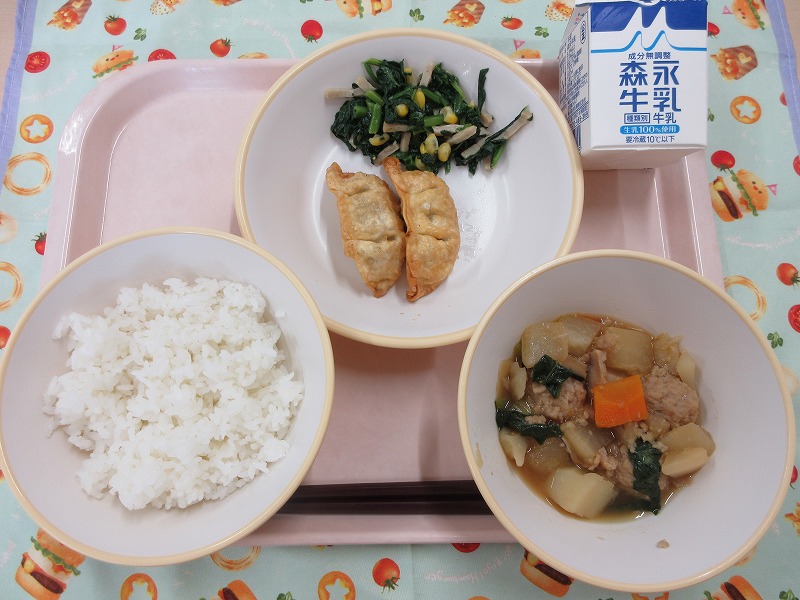ピンクのトレーに給食が右上から反時計回りで牛乳、揚げ餃子とポパイサラダ、ご飯、根菜と肉だんごの煮物と並べられている写真