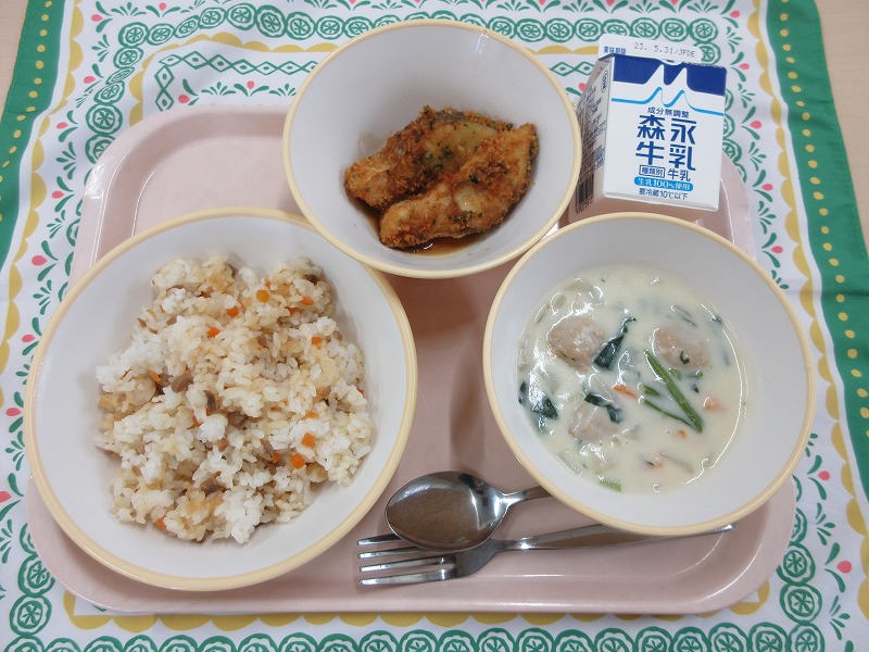 ピンクのトレーに給食が右上から反時計回りで牛乳、白身魚のフライ、ガーリックライス、ミートボールのクリームシチューと並べられている写真