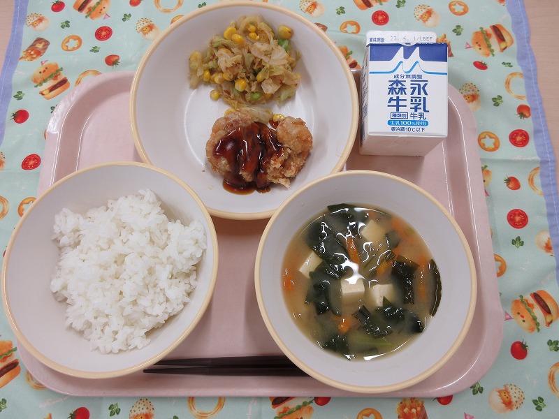 ピンクのトレーに給食が右上から反時計回りで牛乳、鶏肉のかりん揚げとキャベツのおかか和え、ご飯、味噌汁と並べられている写真