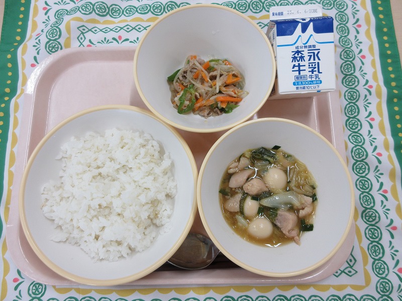 ピンクのトレーに給食が右上から反時計回りで牛乳、春雨の五目炒め、麺もち麦入りご飯、ねぎま丼と並べられている写真
