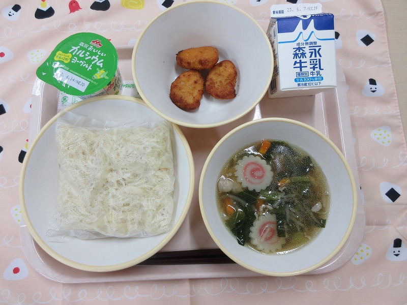 ピンクのトレーに給食が右上から反時計回りで牛乳、チキンナゲット、ヨーグルト、麺、しょうゆラーメンと並べられている写真