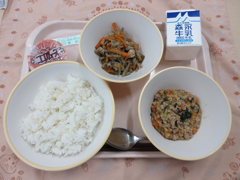 ピンクのトレーに給食が右上から反時計回りで牛乳、きんぴらごぼう、ココアムース、もち麦入りごはん、肉みそ丼と並べられている写真