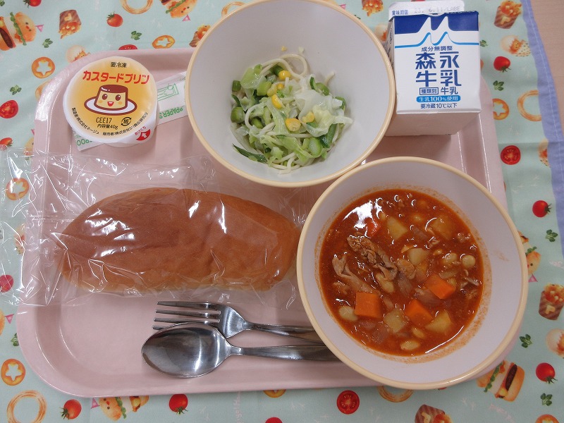 ピンクのトレーに給食が右上から反時計回りで牛乳、グリーンサラダ、カスタードプリン、コッペパン、ポークビーンズと並べられている写真