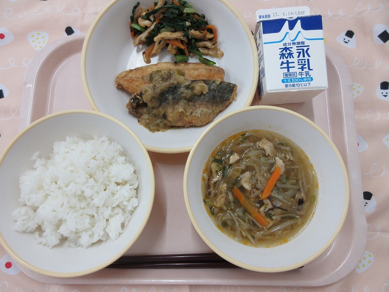 ピンクのトレーに給食が右上から反時計回りで牛乳、あじの梅みそだれと小松菜のおひたし、ごはん、切り干し大根のピリ辛スープと並べられている写真