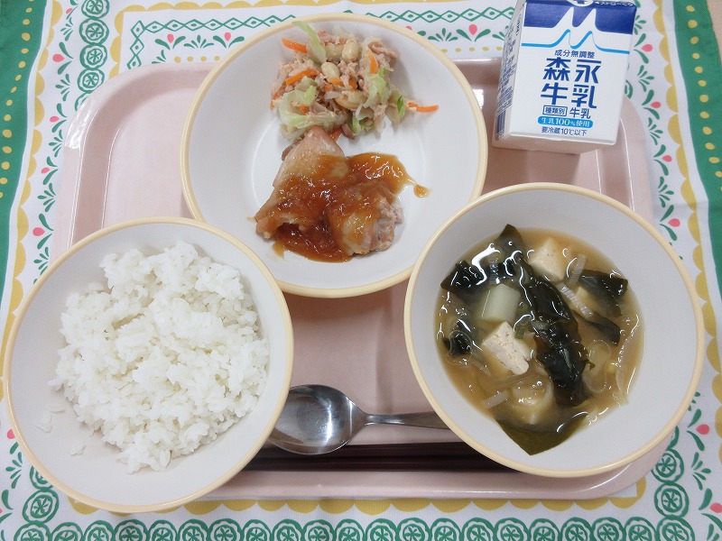 ピンクのトレーに給食が右上から反時計回りで牛乳、鶏肉の生姜焼きとまめツナサラダ、ごはん、じゃがいもの味噌汁と並べられている写真