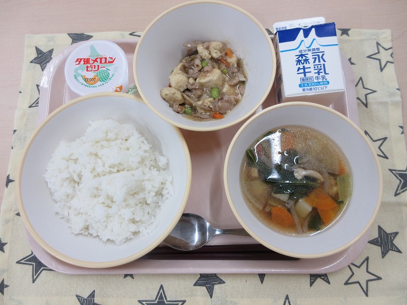 ピンクのトレーに給食が右上から反時計回りで牛乳、肉豆腐あんかけ丼、メロンゼリー、ごはん、鶏けんちん汁と並べられている写真