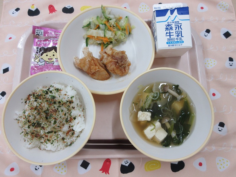 ピンクのトレーに給食が右上から反時計回りで牛乳、鶏肉の甘酢だれとうま塩キャベツ、ごはん（おかかふりかけ）、すまし汁と並べられている写真