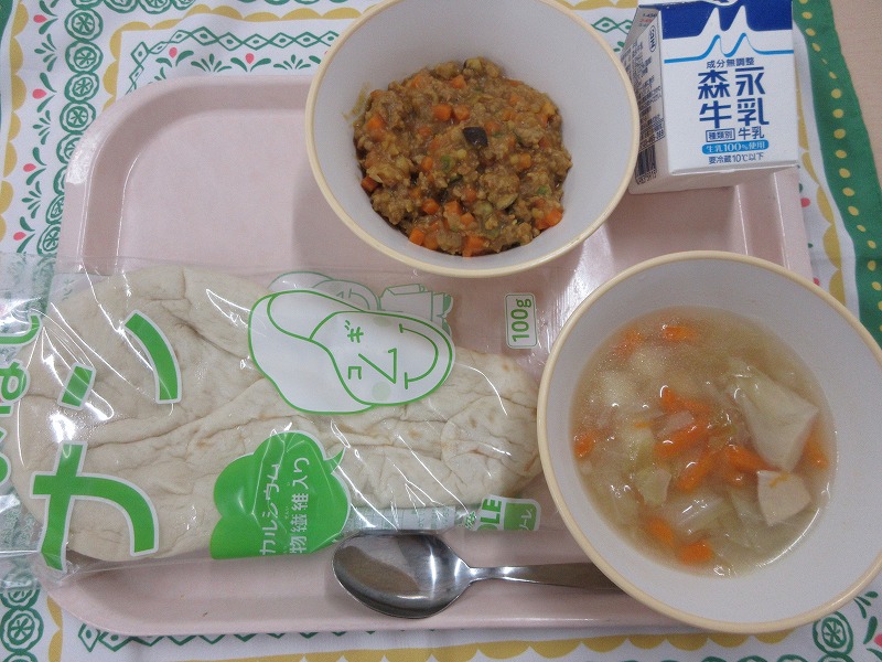 ピンクのトレーに給食が右上から反時計回りで牛乳、キーマカレー、ナン、野菜スープと並べられている写真