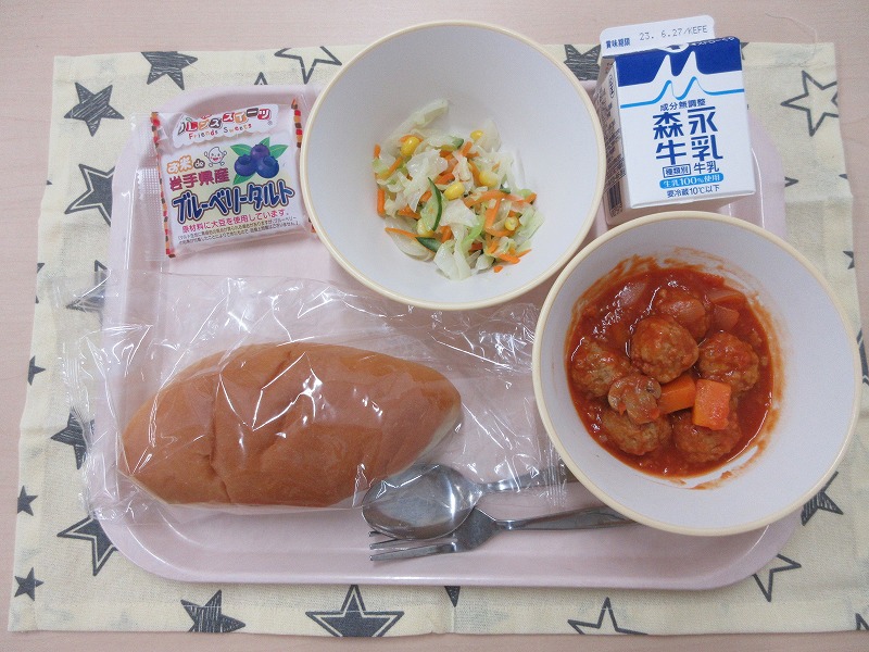 ピンクのトレーに給食が右上から反時計回りで牛乳、コールスローサラダ、ブルーベリータルト、ソフトフランスパン、ミートボールのトマト煮と並べられている写真