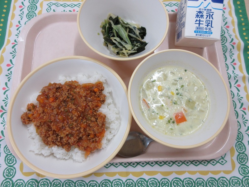 ピンクのトレーに給食が右上から反時計回りで牛乳、海藻サラダ、タコライス、コーンのミルクスープと並べられている写真