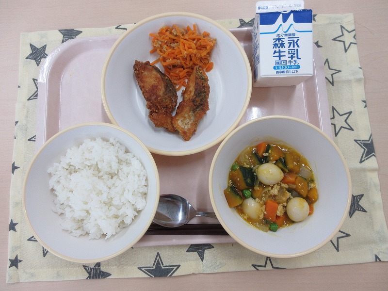 ピンクのトレーに給食が右上から反時計回りで牛乳、白身魚のカレー揚げとにんじんしりしり、ごはん、かぼちゃのそぼろ煮と並べられている写真