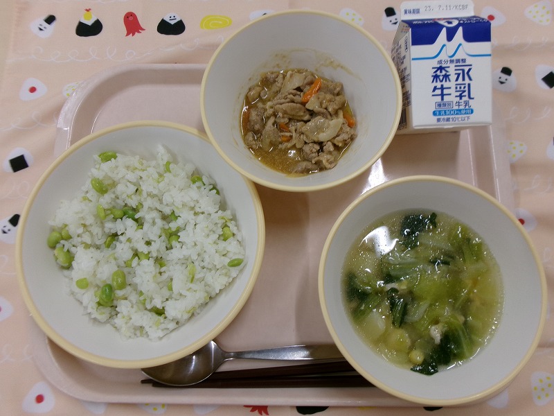 ピンクのトレーに給食が右上から反時計回りで牛乳、豚肉のみそ炒め、枝豆おこわ、キャベツのスープと並べられている写真