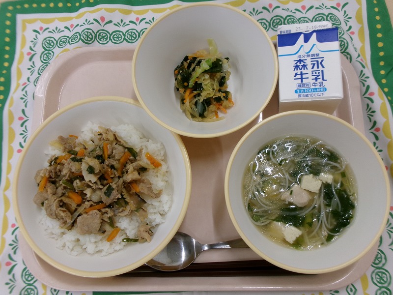 ピンクのトレーに給食が右上から反時計回りで牛乳、海藻サラダ、焼肉ごはん、ビーフンスープと並べられている写真