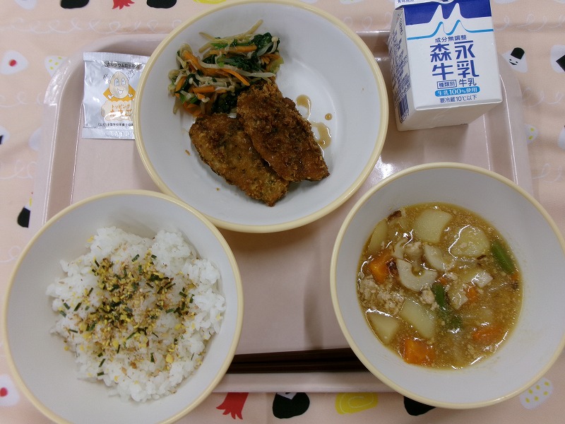 ピンクのトレーに給食が右上から反時計回りで牛乳、あじフライとナムル、ごはん（たまごふりかけ）、じゃがいものそぼろ煮と並べられている写真