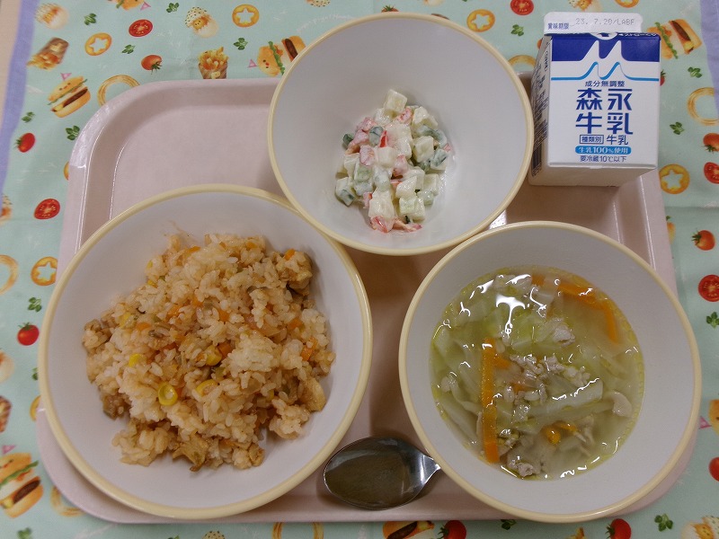 ピンクのトレーに給食が右上から反時計回りで牛乳、マセドアンサラダ、チキンライス、スコッチブロスと並べられている写真