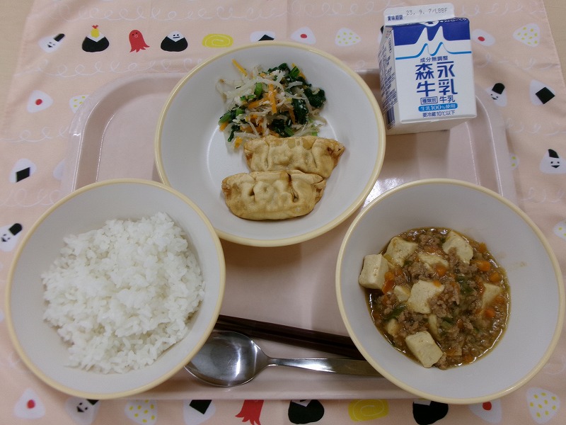 ピンクのトレーに給食が右上から反時計回りで牛乳、揚げ餃子とささみ入りナムル、ご飯、麻婆豆腐と並んでいる写真