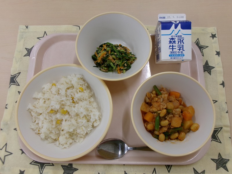 ピンクのトレーに給食が右上から反時計回りで牛乳、こまツナサラダ、コーンピラフ、ポークビーンズと並んでいる写真