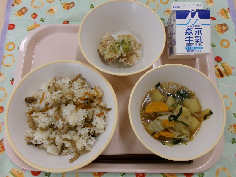 ピンクのトレーに給食が右上から反時計回りで牛乳、ねぎ塩だれから揚げ、五目まぜごはん、野菜の旨煮と並んでいる写真