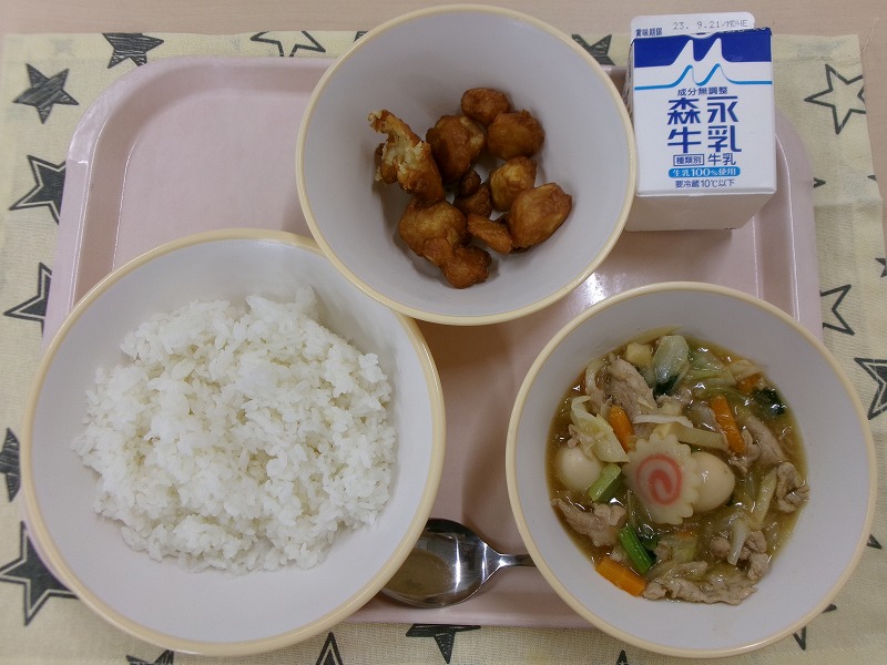 ピンクのトレーに給食が右上から反時計回りで牛乳、あげいも、ご飯、中華あんと並んでいる写真