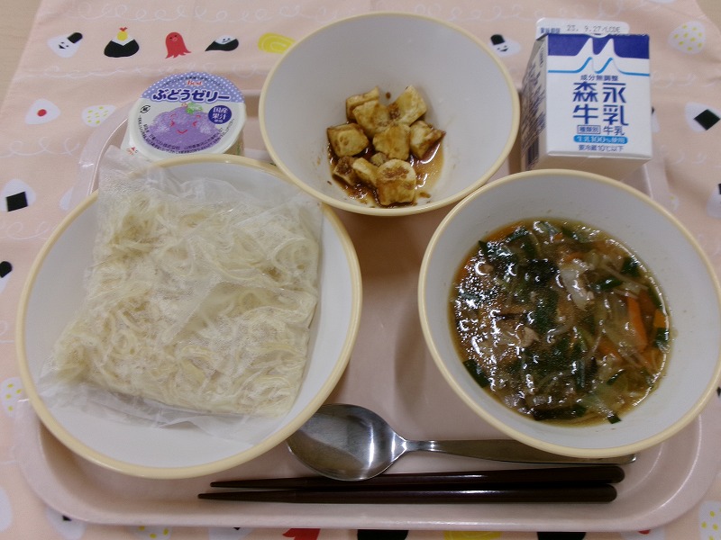 ピンクのトレーに給食が右上から反時計回りで牛乳、じゃがいものごまだれかけ、ぶどうゼリー、サンマーメン、サンマーメンの具と並んでいる写真