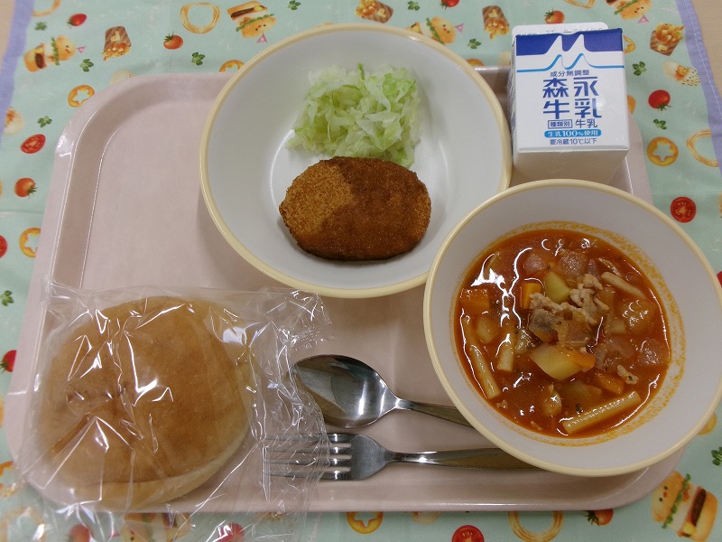 ピンクのトレーに給食が右上から反時計回りで牛乳、コロッケとキャベツ、パン、ミネストローネと並んでいる写真