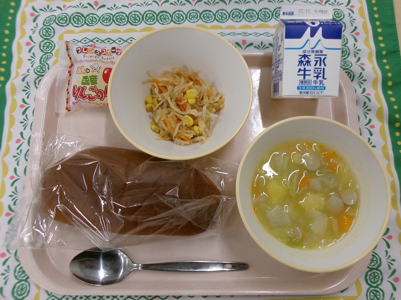 ピンクのトレーに給食が右上から反時計回りで牛乳、切り干し大根とチキンのサラダ、りんごタルト、黒パン、ポトフと並んでいる写真