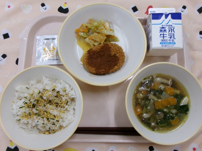 ピンクのトレーに給食が右上から反時計回りで牛乳、コロッケとキャベツと生揚げの炒め物、麦入りごはん（ふりかけ）、芋の子汁と並んでいる写真