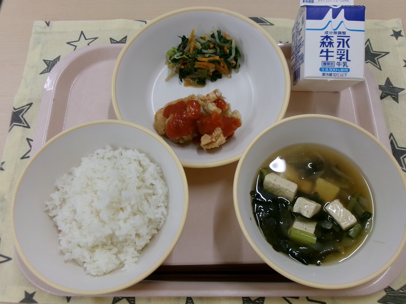 ピンクのトレーに給食が右上から反時計回りで牛乳、鶏チリとナムル、ご飯、豆腐のスープと並んでいる写真