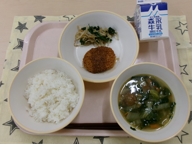 ピンクのトレーに給食が右上から反時計回りで牛乳、メンチカツともやしのおかか和え、ご飯、白菜と肉団子のスープと並んでいる写真