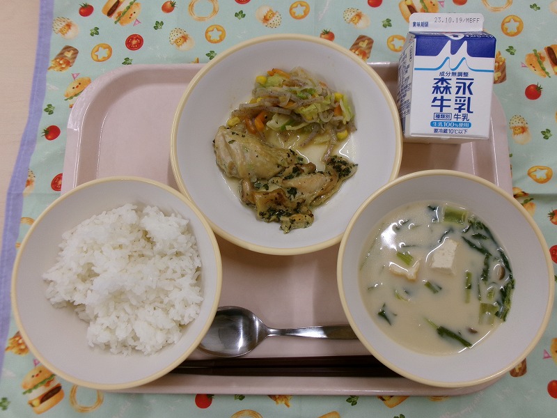 ピンクのトレーに給食が右上から反時計回りで牛乳、鶏肉のハーブ焼きとこんにゃくソテー、ご飯、ミルクみそスープと並んでいる写真