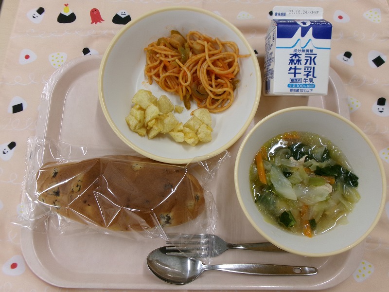 ピンクのトレーに給食が右上から反時計回りで牛乳、スパゲティナポリタンとカレー風味ポテト、ぶどうパン、キャベツのスープと並んでいる写真