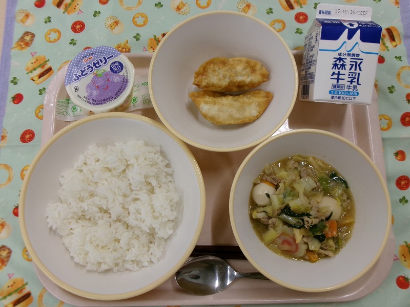 ピンクのトレーに給食が右上から反時計回りで牛乳、揚げ餃子、ぶどうゼリー、ご飯、中華丼と並んでいる写真